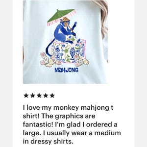 K&ouml;nnte beinhalten: Wei&szlig;es T-Shirt mit einem blauen Affen, der Mahjong spielt und einen gr&uuml;nen Sonnenschirm h&auml;lt. Das Design zeigt Mahjong-Steine und das Wort "MAHJONG". Ein lustiges und einzigartiges Grafik-T-Shirt.