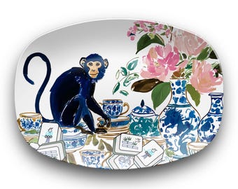 May include: An oval serving platter with a whimsical design. A blue monkey sits among blue and white teacups, teapots, and vases. Pink flowers and mahjong tiles complete the scene. The platter has a white background.