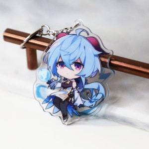 May include: A blue and white anime character keychain with a blue and white background. The character is a young woman with long blue hair and a white dress. She is holding a blue orb in her hand.