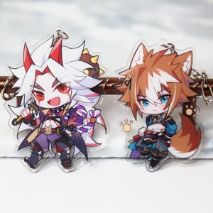 Peut inclure: Deux porte-clés de personnages de style anime. Le porte-clés de gauche représente un personnage aux cheveux blancs avec des yeux rouges et des cornes, portant une tenue violette et dorée. Le porte-clés de droite représente un personnage aux cheveux bruns avec des yeux bleus et des oreilles de renard, portant une tenue bleue et dorée.