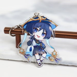 May include: A blue and gold anime character keychain with a blue hat and a white and blue outfit. The character is smiling and has blue eyes.