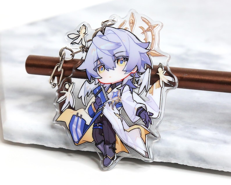 May include: A clear acrylic charm featuring a stylized anime character with light blue hair and a white and blue outfit. The charm has a silver keychain attachment and decorative elements. The character has yellow eyes and is in a dynamic pose.