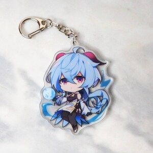 May include: A blue and white anime character keychain with a silver key ring. The character has blue hair and is wearing a white and blue outfit.
