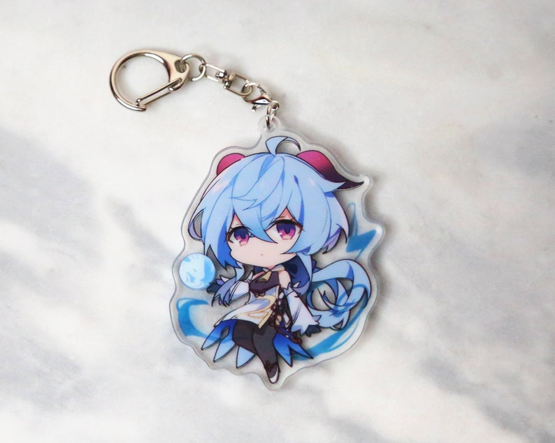 May include: A blue and white anime character keychain with a silver key ring. The character has blue hair and is wearing a white and blue outfit.