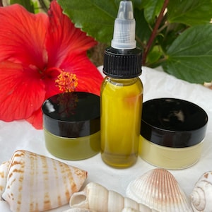 May include: Two small jars of green and yellow cream with a dropper bottle of yellow oil. The jars and bottle are on a white surface with seashells.