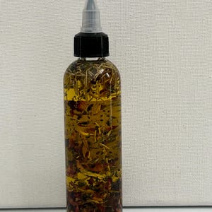 May include: A clear glass bottle with a black cap and a dropper top. The bottle is filled with a yellow liquid and contains various herbs and flowers.