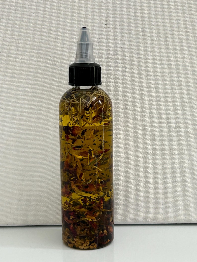 May include: A clear glass bottle with a black cap and a dropper top. The bottle is filled with a yellow liquid and contains various herbs and flowers.