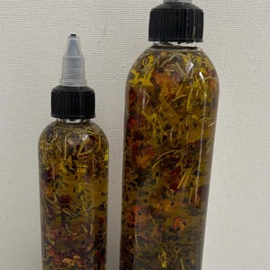 May include: Two clear glass bottles with black caps and droppers filled with a yellow oil infused with dried herbs and flowers.