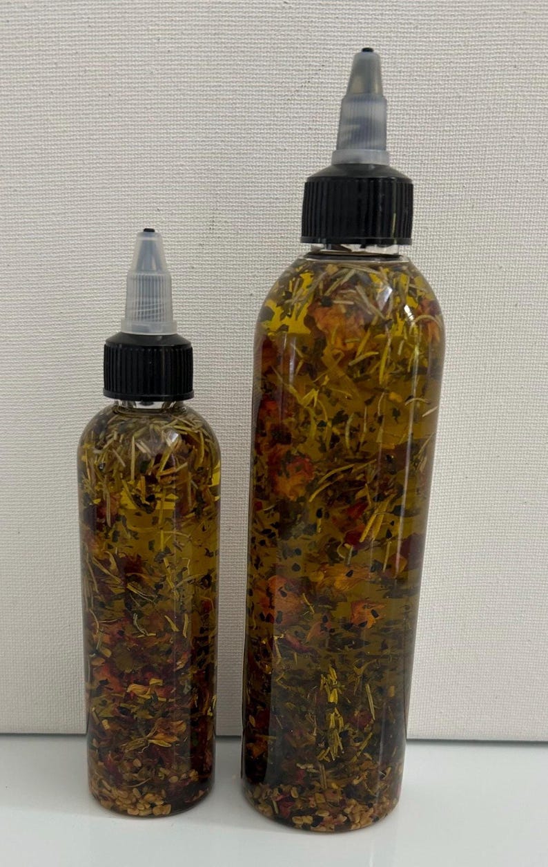 May include: Two clear glass bottles with black caps and droppers filled with a yellow oil infused with dried herbs and flowers.