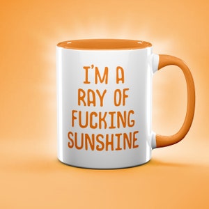 May include: White ceramic mug with an orange rim and handle. The mug has the text "I'm a ray of fucking sunshine" printed in orange.