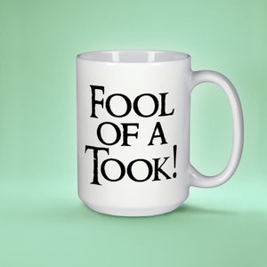 May include: White ceramic mug with a black inscription that reads "Fool of a Took!"