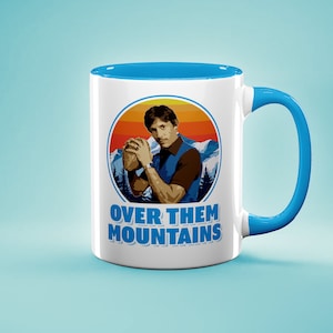 May include: White ceramic coffee mug with a blue rim and handle. The mug features a retro-style illustration of a man holding a football with the text "Over Them Mountains" in blue.