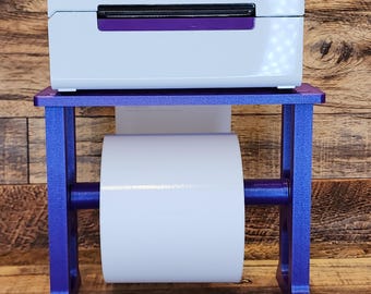 May include: A white label printer with the word "rollo" on the front, sitting on a purple metal stand with a roll of white label paper.