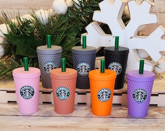 May include: Six colorful plastic tumblers with a Starbucks logo and the words "Starbucks Coffee" printed on them. The tumblers are arranged in a semi-circle on a wooden surface.