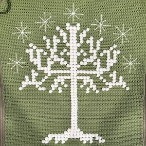 May include: A green crocheted square featuring a white tree design with a detailed trunk and branches. Surrounding the tree are eight white starbursts. The crochet work is visible, adding texture to the design.