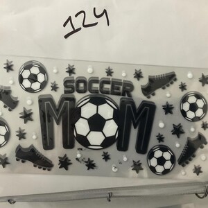 K&ouml;nnte beinhalten: Ein klarer Aufkleberbogen mit Fu&szlig;ball-Motiv. Das Design zeigt die Worte "SOCCER MOM" in Schwarz und Wei&szlig;, Fu&szlig;b&auml;lle, Fu&szlig;ballschuhe, Sterne und kleine wei&szlig;e Kreise. Die Nummer "124" ist handschriftlich oben.
