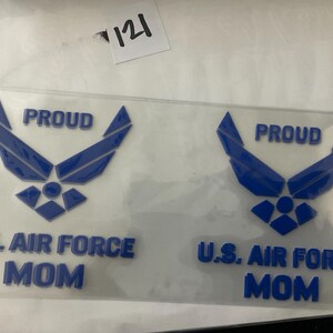 K&ouml;nnte beinhalten: Zwei transparente Aufkleber mit einem blauen US Air Force-Emblem und Text. Die Aufkleber lesen "PROUD" &uuml;ber dem Emblem und "U.S. AIR FORCE MOM" darunter. Die Aufkleber befinden sich auf wei&szlig;em Hintergrund.