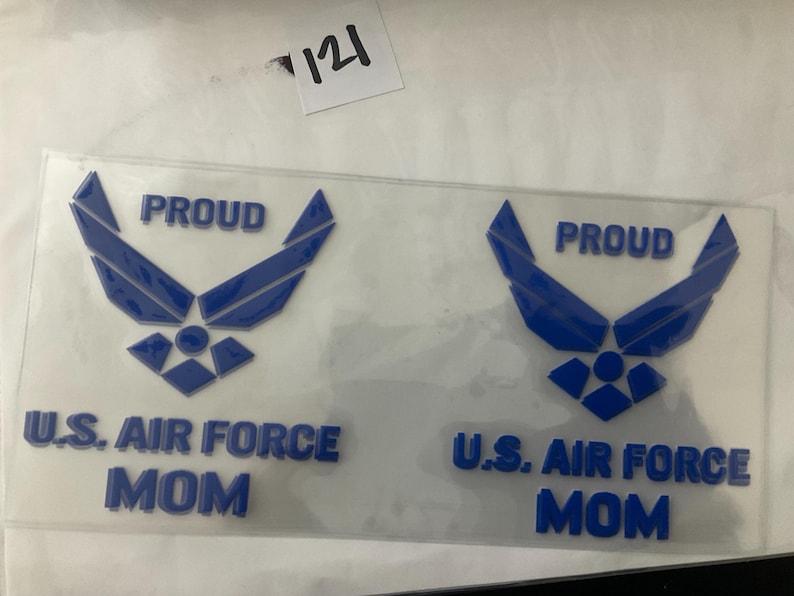 K&ouml;nnte beinhalten: Zwei transparente Aufkleber mit einem blauen US Air Force-Emblem und Text. Die Aufkleber lesen "PROUD" &uuml;ber dem Emblem und "U.S. AIR FORCE MOM" darunter. Die Aufkleber befinden sich auf wei&szlig;em Hintergrund.