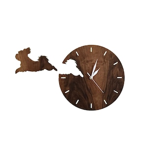 Könnte beinhalten: Eine Wanduhr aus Holz mit einer Silhouette eines Hundes, der durch das Zifferblatt der Uhr läuft. Das Zifferblatt der Uhr ist aus dunklem Holz mit einem weißen Uhrzeiger.