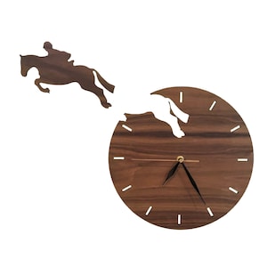 May include: A wooden wall clock with a silhouette of a horse and rider jumping over an obstacle. The clock face is brown with black hands and white markings.
