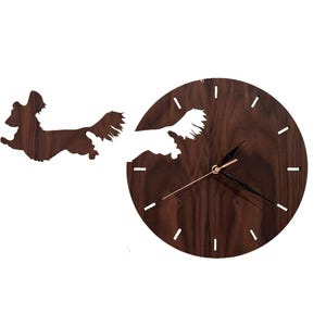 Könnte beinhalten: Eine braune Holzuhr mit einer Silhouette eines Hundes, der durch das Zifferblatt der Uhr läuft. Die Zeiger der Uhr sind golden.