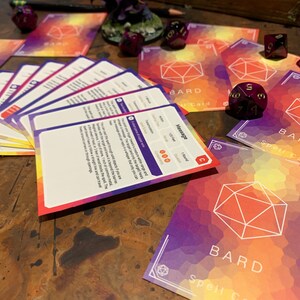 Pu&ograve; includere: Un set di carte di incantesimi colorate per un gioco di ruolo fantasy. Le carte presentano un'icona di dado bianca su uno sfondo viola, arancione e giallo. Il testo sulle carte recita "Carta di incantesimo del bardo".