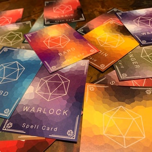 May include: A close-up of a pile of colorful cards with a white geometric design. The cards are labeled with different character classes, such as "Wizard", "Bard", "Warlock", and "Ranger".