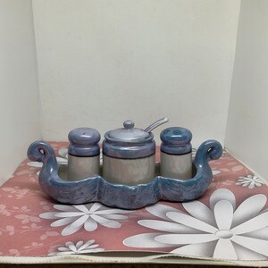 Op de afbeelding: Een keramische zout- en peperstrooierset met een bijpassend condimentenschotel. De set is versierd met een blauw en wit swirl-patroon en heeft een schotel in de vorm van een boot.