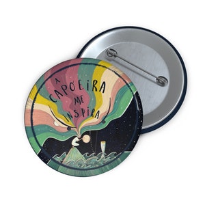 May include: A round button with a colorful illustration of a person doing capoeira. The text "A CAPOEIRA ME INSPIRA" is written in a stylized font around the person.