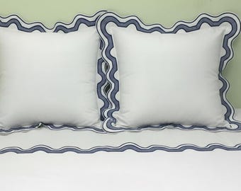 Pode incluir: Duas almofadas quadradas brancas com uma borda ondulada azul marinho, repousando sobre uma colcha branca com borda correspondente. O conjunto de roupa de cama oferece um visual limpo e clássico.