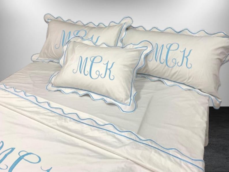 May include: White bed linens with blue scalloped trim and embroidered initials "MCK".