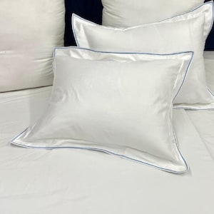 May include: Two white pillowcases with a light blue trim. The pillowcases are on a white bed.