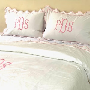 May include: White bedding with pink scalloped edges and pink embroidered initials "PDS" on the pillows and duvet cover.