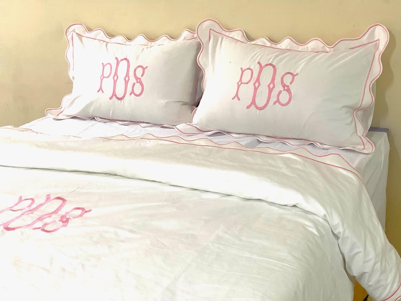 May include: White bedding with pink scalloped edges and pink embroidered initials "PDS" on the pillows and duvet cover.