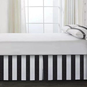 May include: A white bed with a black and white striped bed skirt. The bed has a white headboard and two white pillows with black stripes.