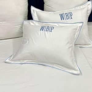 May include: Two white pillowcases with blue piping and the text "WIBIP" embroidered in blue on each pillowcase.
