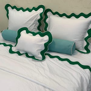 May include: White bedding set with green scalloped trim. The set includes two square pillows, a smaller square pillow, and a bolster pillow in a light blue color. The bedspread also features the green scalloped trim.