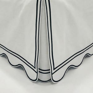 May include: White fabric with a scalloped edge and black trim. The fabric has a folded design with a black border and a scalloped edge. The design is simple and elegant, suitable for home decor.