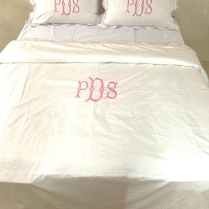 May include: White bedding set with pink scalloped edges and pink embroidered initials "PDS" on the pillowcases and duvet cover.