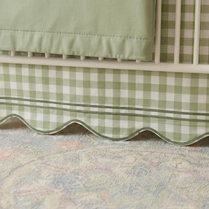 May include: A cot with a light green and white gingham patterned skirt and sheet. The skirt has a scalloped edge with a double-stitched border. The cot is white.