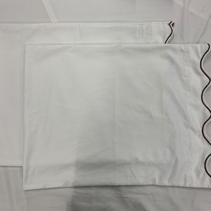 Könnte beinhalten: Zwei weiße Kissenbezüge mit einem gewellten Rand und einem dünnen roten Besatz.