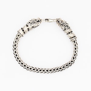 Peut inclure: Un bracelet en argent avec une cha&icirc;ne tress&eacute;e et des accents de t&ecirc;te de dragon.