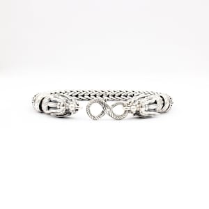 Peut inclure: Un bracelet en argent avec des fermoirs en t&ecirc;te de dragon et un symbole d'infini au centre.