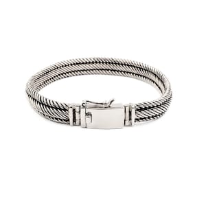 May include: A silver-toned bracelet featuring a multi-strand twisted cable design. The piece is secured with a rectangular box clasp that includes a hinged safety latch, providing a polished and uniform metallic finish throughout the entire structure.