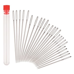 May include: A set of twenty-four silver-toned metal sewing needles with elongated eyes, arranged in a fan shape, accompanied by a clear cylindrical plastic storage tube featuring a bright red screw-on cap for secure organization and storage.