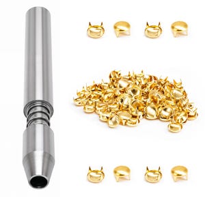 Könnte beinhalten: Ein silberfarbenes Metall-Setzwerkzeug mit Federmechanismus neben einer großen Ansammlung kleiner, runder, goldfarbener Metallnieten, die an der Unterseite vier Zacken zur Befestigung an Stoff oder Leder aufweisen.