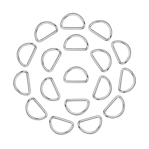May include: A collection of silver-colored D-rings arranged in a circular pattern against a white background. The D-rings are made of metal and have a smooth, shiny finish. They are commonly used in various crafting and hardware applications.