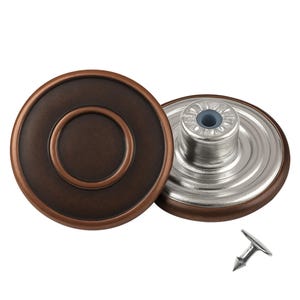 May include: Two bronze-coloured jean buttons with silver metal backing and a small silver tack are shown. The buttons have a circular design with a raised outer ring and a smaller inner circle. The tack is small and pointed.