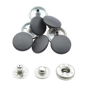 May include: A selection of black snap fasteners with silver metal backings. The snaps have a round, flat design. Three different styles of the snap backing are also shown.