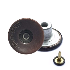 May include: Close-up of three denim buttons. The buttons are a dark bronze colour with the words "UTILITY DENIM" embossed around the edge. One button is detached, showing the post and back.
